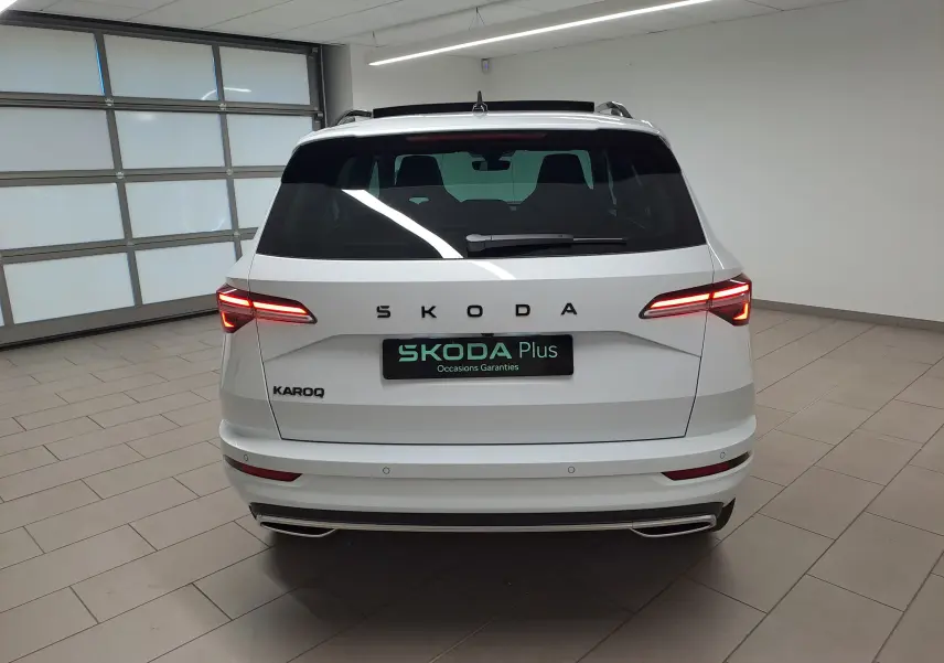 Vue arrière d'un Skoda Karoq blanc lune 2025 avec feux allumés dans un showroom lumineux.