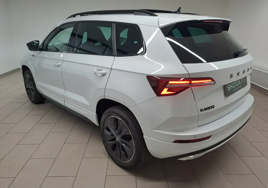 Vue 3/4 arrière droite du Skoda Karoq blanc Lune avec feux allumés et jantes noires sportline.