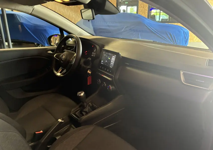 Vue intérieure côté conducteur de la Renault Clio 1.5 BlueDCI Business 2022 avec tableau de bord noir et boîte manuelle.