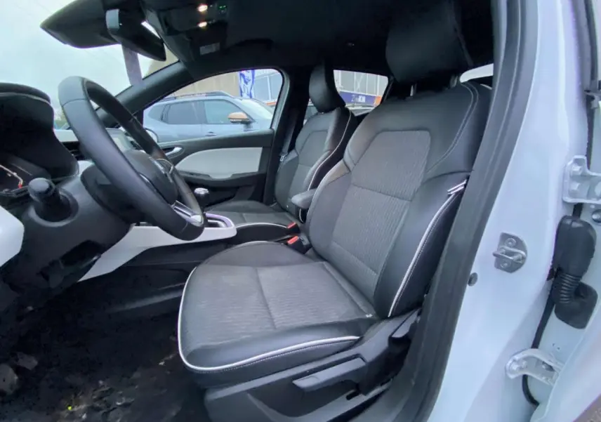 Vue intérieure côté conducteur d'une Renault Clio blanche 2023 avec sièges similicuir gris et tableau de bord moderne.