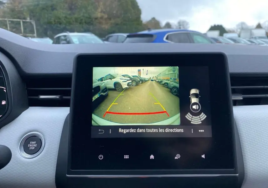 Vue intérieure sur l'écran tactile affichant la caméra de recul d'une Renault Clio blanche avec tableau de bord gris.
