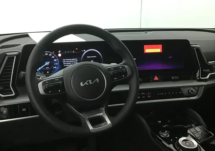 Vue intérieure centrée sur le volant noir du Kia Sportage 2025 avec tableau de bord digital et écran tactile large.