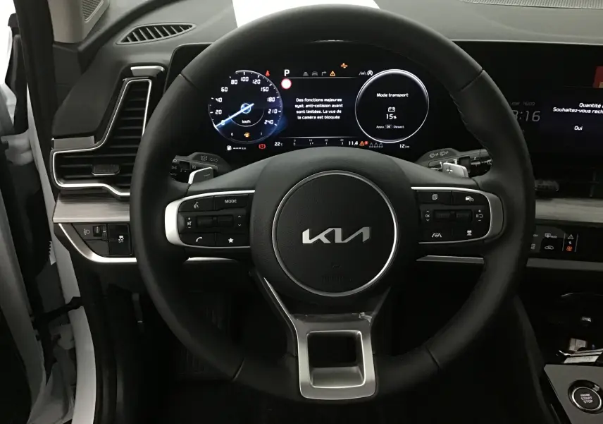 Vue rapprochée du volant noir du Kia Sportage 2025 avec combiné d'instrumentation digital et écran tactile.
