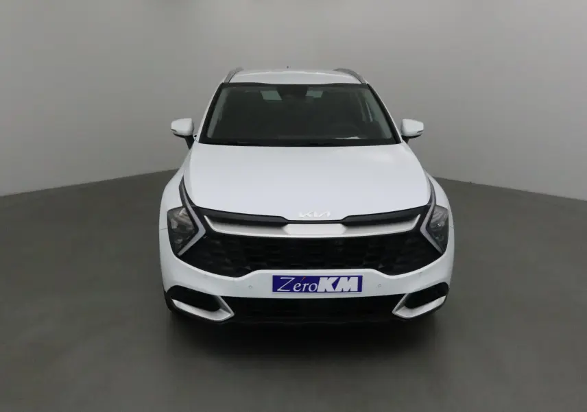 Vue frontale d'un Kia Sportage blanc 2025 avec calandre noire et logo Kia moderne sur fond neutre.