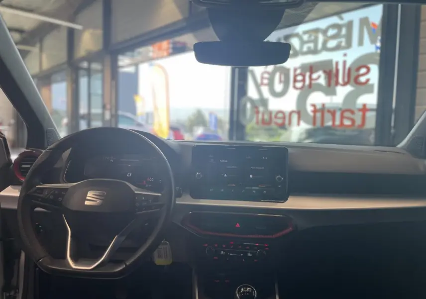 Vue intérieure avant du SEAT Arona 2024 avec tableau de bord noir, volant sport cuir et écran tactile central.