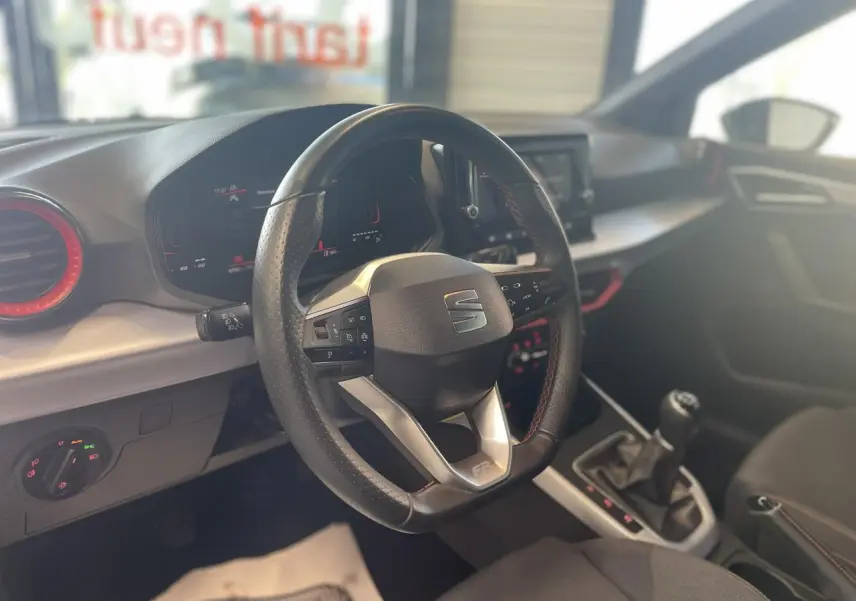 Intérieur du SEAT Arona 2024 vu côté conducteur, volant sport cuir noir avec surpiqûres rouges et tableau de bord digital.