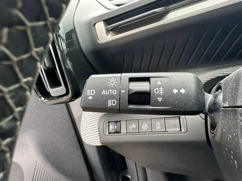 Gros plan sur la commande des feux et clignotants à gauche du volant dans l’habitacle gris d’une Citroën C3 2025.