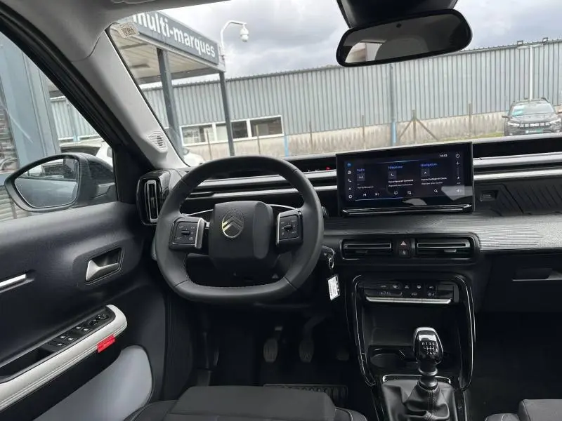 Vue intérieure avant du Citroën C3 2025 gris Mercury, avec volant multifonction et écran tactile central.