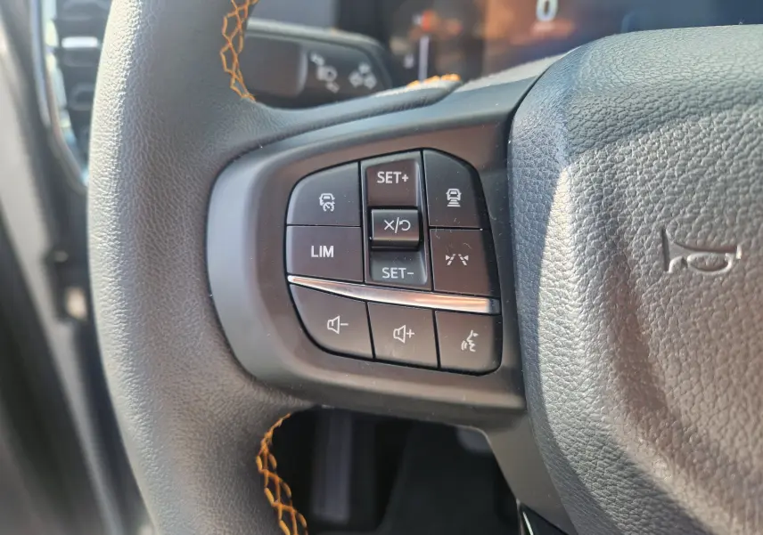 Gros plan sur les commandes au volant du Ford Ranger Super Cabine gris Iconic, avec surpiqûres orange visibles.