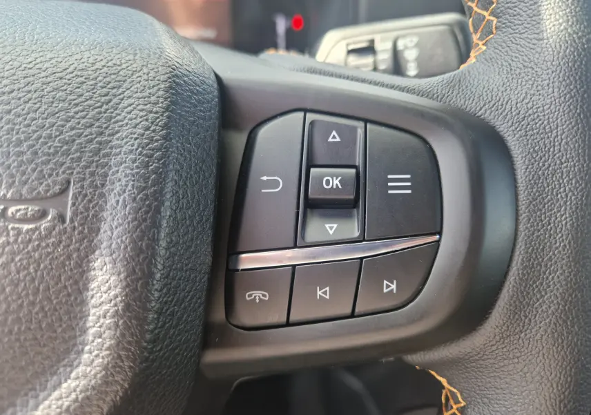 Gros plan sur les commandes multifonctions à droite du volant en cuir noir avec surpiqûres orange du Ford Ranger Wildtrak 2025.