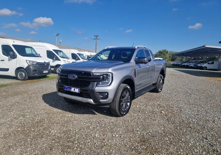 Ford Ranger Super Cabine gris iconic en 3/4 avant droit sur un terrain gravillonné avec plusieurs utilitaires blancs en arrière-plan.