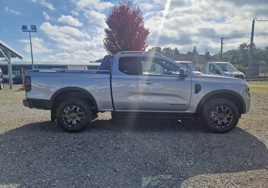 Ford Ranger Wildtrak gris iconic vu de profil côté gauche sur un sol gravillonné avec benne protégée.