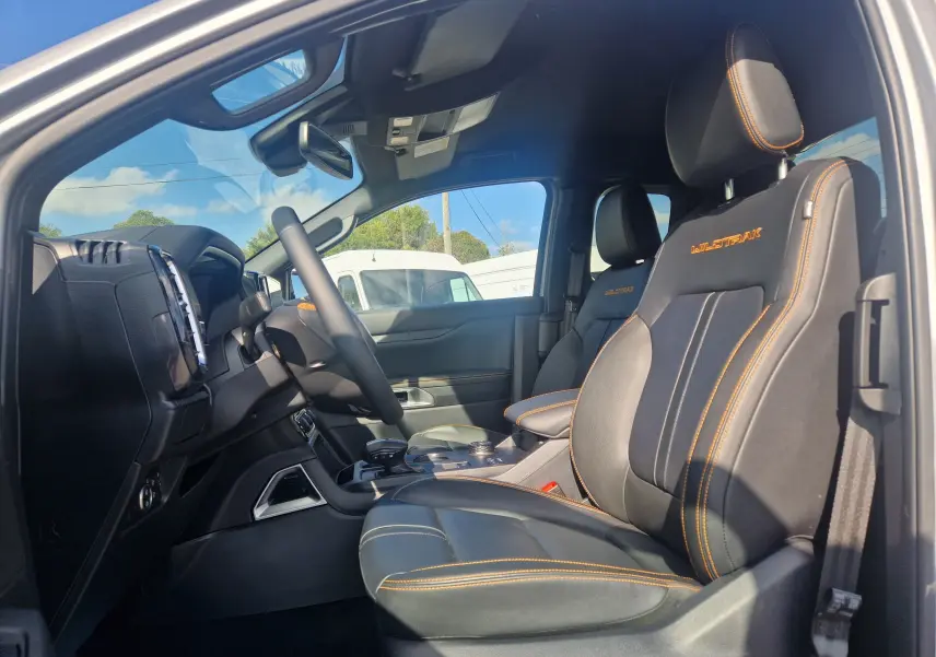 Vue intérieure côté conducteur du Ford Ranger Super Cabine Wildtrak 2025, sièges cuir noirs avec surpiqûres orange et logo brodé.