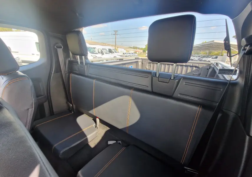 Vue intérieure arrière du Ford Ranger Super Cabine 2025, sièges noirs avec surpiqûres orange et vitre arrière donnant sur la benne.