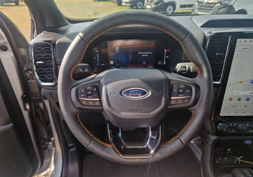 Vue centrée sur le volant cuir noir avec surpiqûres orange du Ford Ranger Wildtrak 2025, tableau de bord digital et écran tactile.
