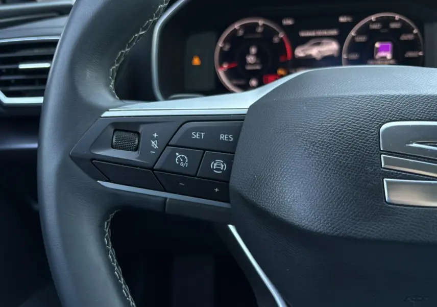 Gros plan sur le volant cuir multifonction gris foncé du SEAT Leon 2024 avec commandes de régulateur et affichage digital en arrière-plan.