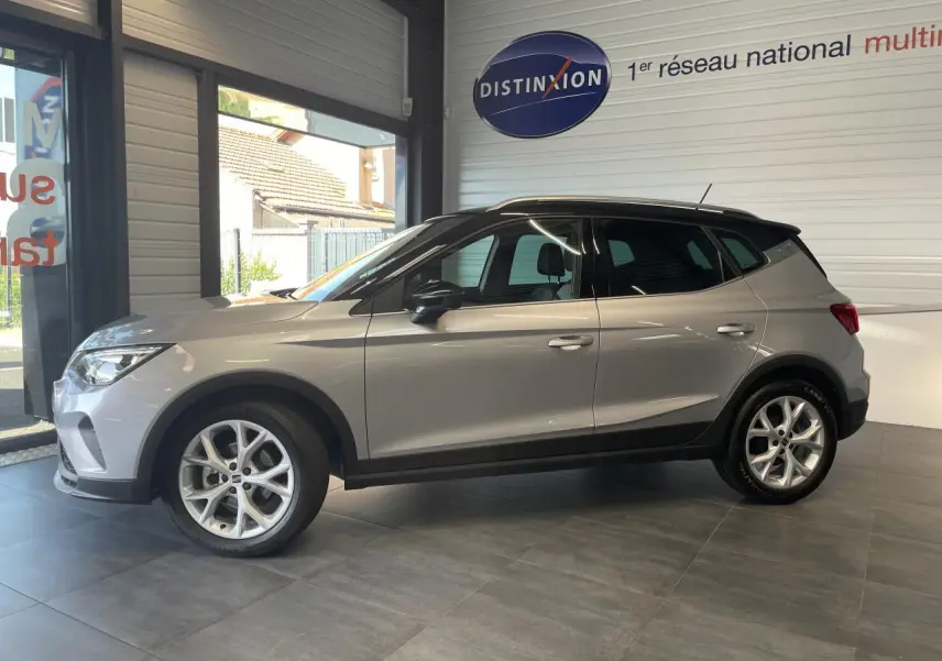 SEAT Arona 2024 gris clair en profil droit, avec toit noir et jantes alliage 16 pouces en showroom.