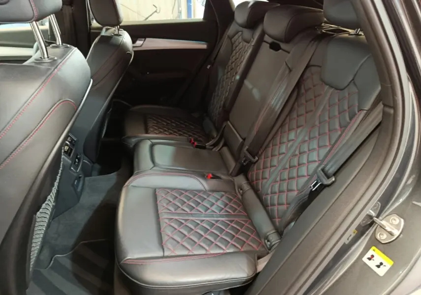 Vue intérieure côté droit des sièges arrière en cuir noir avec surpiqûres rouges de l'Audi Q5 gris clair 2023 hybride rechargeable.
