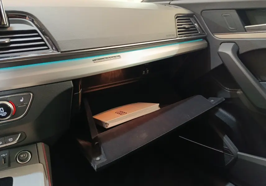 Intérieur de l'Audi Q5 2023 gris clair, vue sur la boîte à gants ouverte côté passager avec manuel Audi visible.