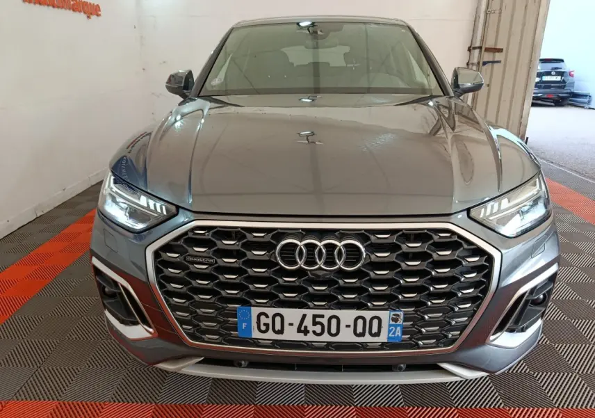 Vue avant d’un Audi Q5 gris clair 2023 hybride rechargeable, mettant en valeur sa calandre hexagonale et ses phares LED allumés.