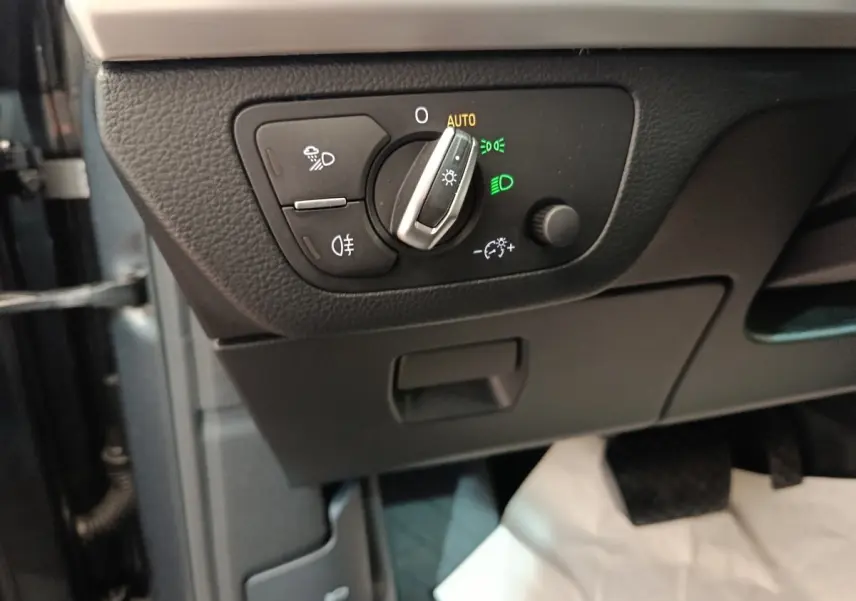 Gros plan sur le bouton de commande des phares avec réglage automatique dans l'Audi Q5 gris clair 2023 hybride rechargeable.