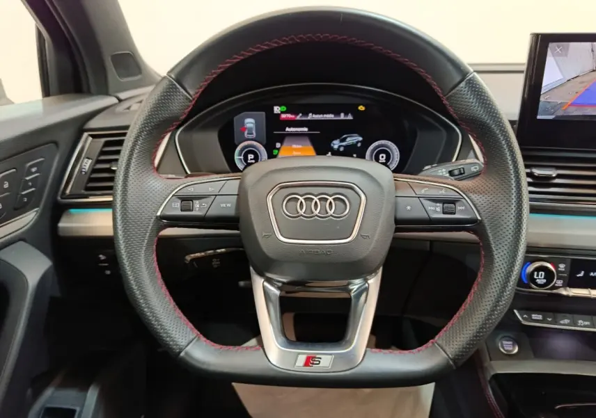 Vue centrée sur le volant perforé avec surpiqûres rouges de l'Audi Q5 2023 hybride rechargeable, tableau de bord digital visible.