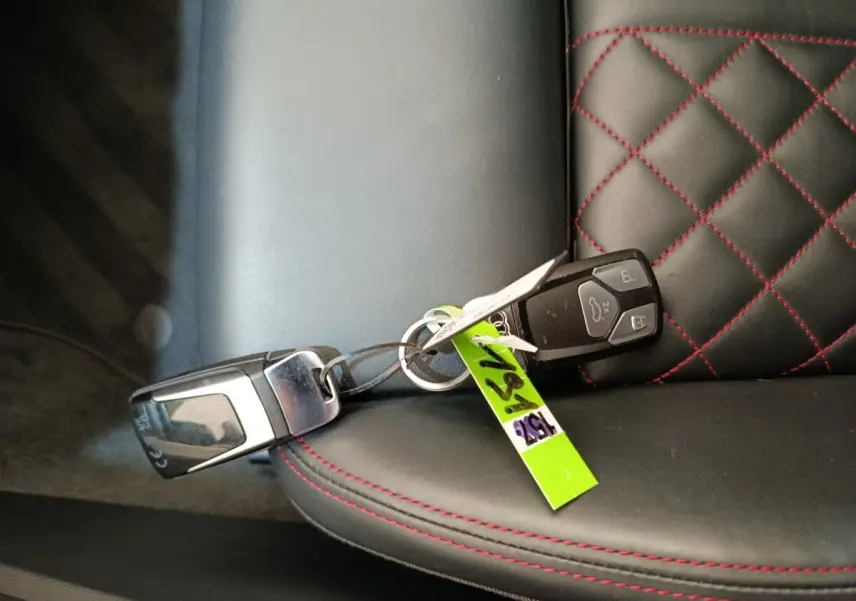 Clé de voiture Audi Q5 2023 hybride rechargeable posée sur un siège cuir noir avec surpiqûres rouges en losange.