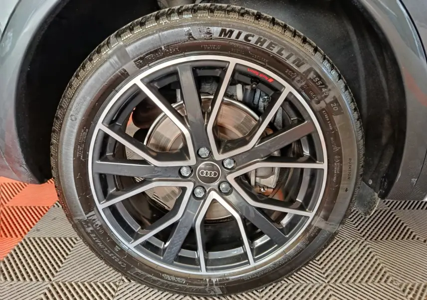 Gros plan sur la roue avant droite d’un Audi Q5 gris clair 2023 avec jante alliage noir et logo Audi au centre.