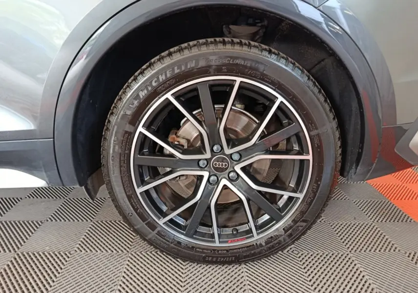 Gros plan sur la roue avant droite gris clair d’un Audi Q5 2023 avec jante noire à branches fines et logo Audi central.