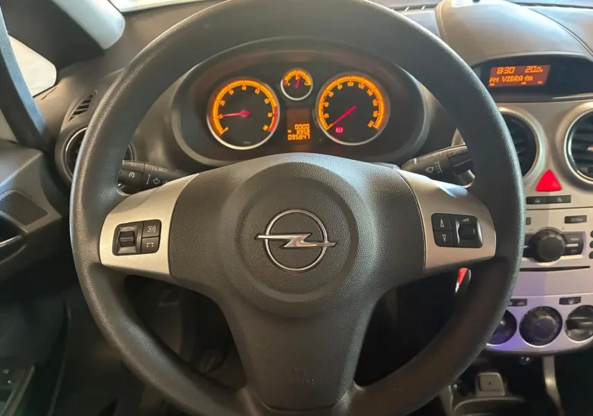 Vue intérieure centrée sur le volant noir d'une Opel Corsa 2012 avec tableau de bord et commandes visibles.
