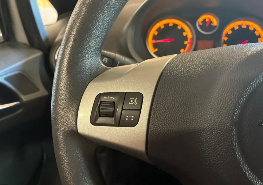 Gros plan sur le volant noir de l'Opel Corsa 2012, avec commandes intégrées et tableau de bord éclairé en orange.
