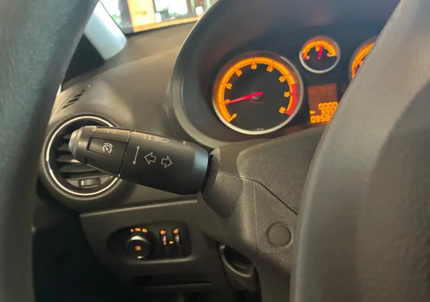 Gros plan sur le commodo gauche et le tableau de bord éclairé orange d'une Opel Corsa gris clair, vue depuis le siège conducteur.