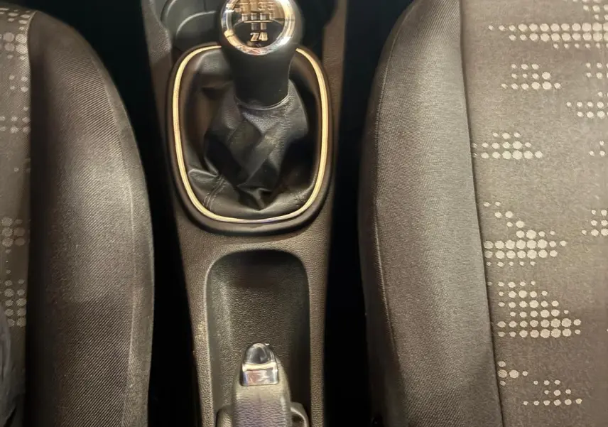 Vue plongeante sur la console centrale d'une Opel Corsa gris clair, mettant en valeur le levier de vitesse manuel et les sièges en tissu noir.