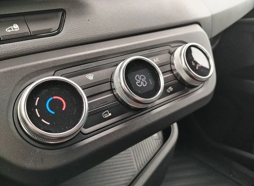 Gros plan sur les commandes de climatisation du Nissan Interstar Fourgon blanc, avec réglages circulaires argentés et tableau de bord noir.