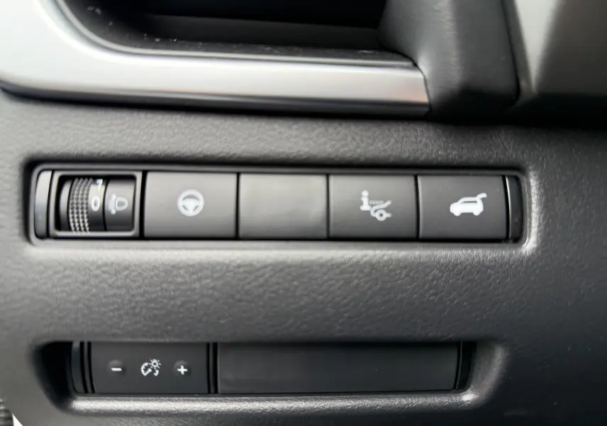 Gros plan sur les commandes noires du tableau de bord du Nissan Qashqai blanc nacré, avec boutons de réglage et ouverture du coffre.
