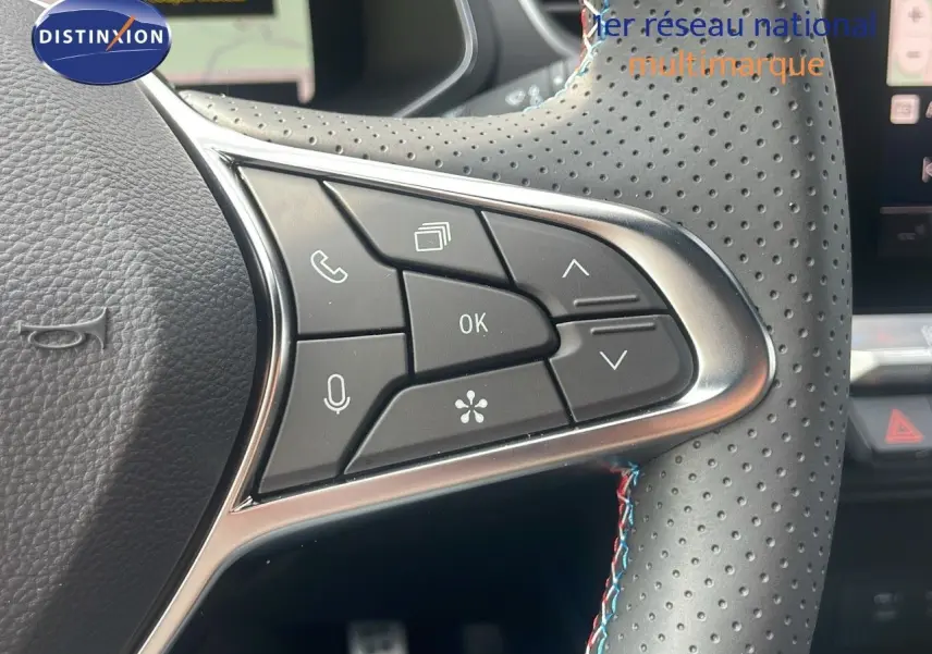 Gros plan sur les commandes du volant perforé avec surpiqûres tricolores du Renault Captur gris Cassiopée 2025.