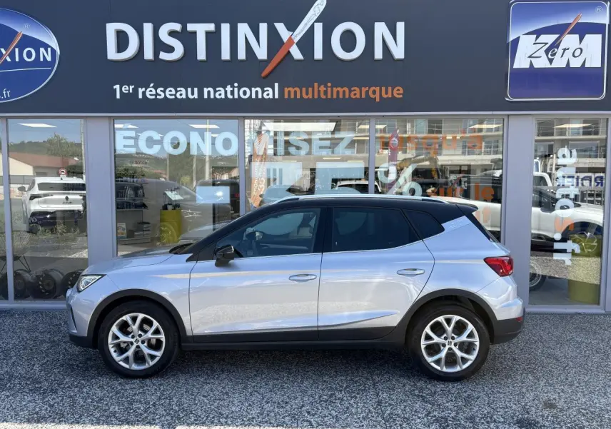 Vue latérale droite du SEAT Arona 2024 en gris clair avec toit noir et jantes alliage 16 pouces devant un showroom.