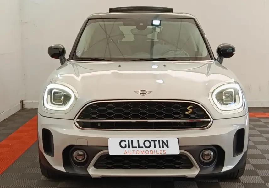 Vue avant d'une MINI Countryman Cooper SE blanche avec phares LED allumés et calandre noire à motif nid d'abeille.