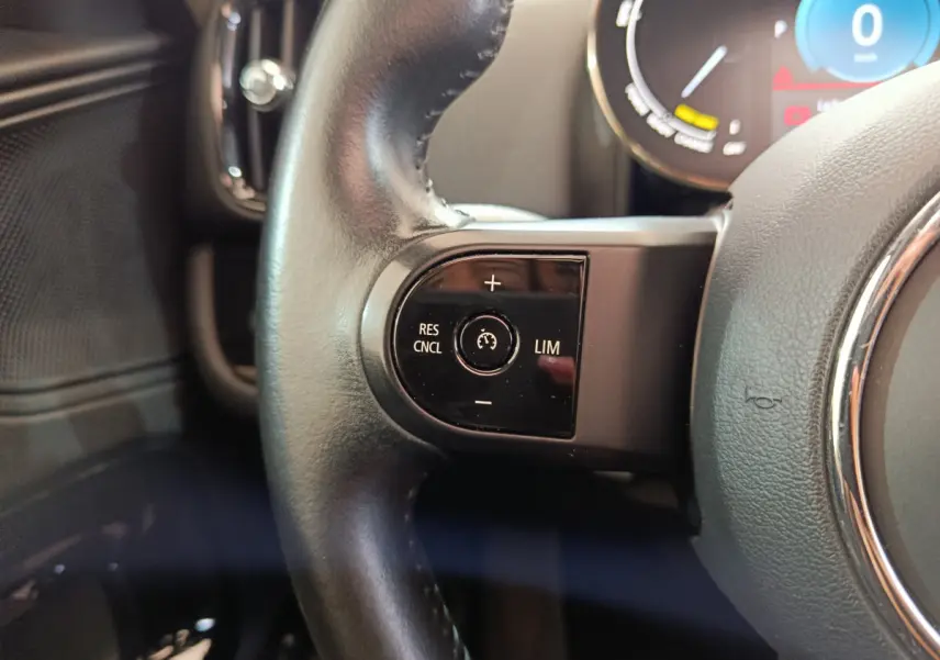 Gros plan sur les commandes de régulateur de vitesse au volant cuir noir d’un MINI Countryman hybride blanc.