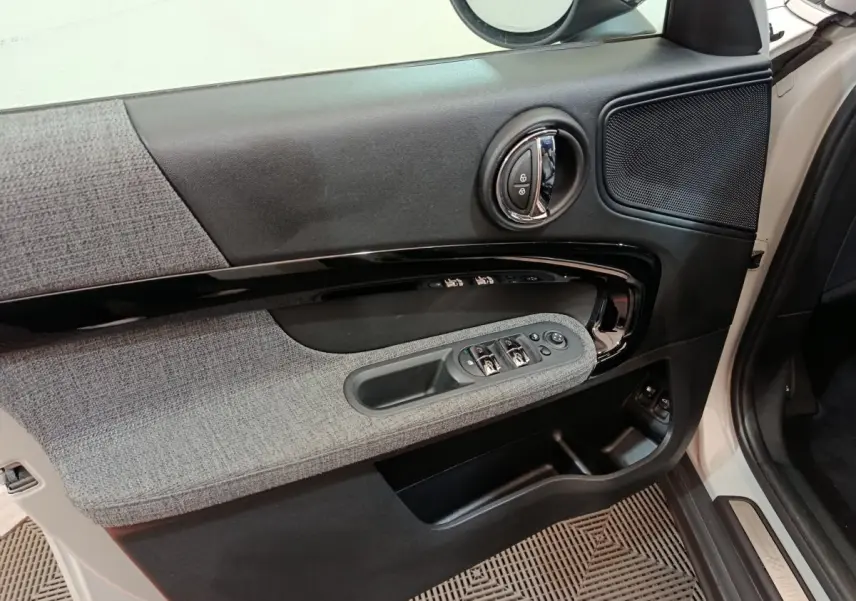 Intérieur côté conducteur du MINI Countryman blanc, montrant la porte avec commandes des vitres et tissu gris.