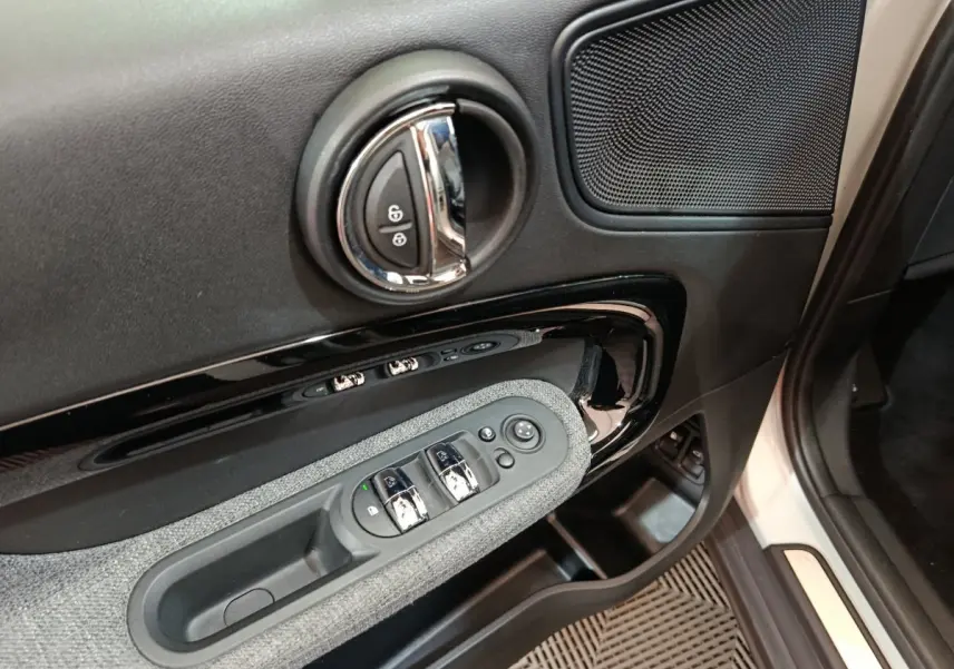 Vue rapprochée de la porte côté conducteur du MINI Countryman blanc, avec commandes de vitres et poignée chromée.