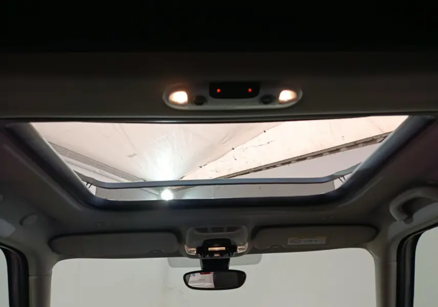 Toit ouvrant panoramique ouvert vu de l'intérieur avant du MINI Countryman blanc, éclairage intérieur allumé.