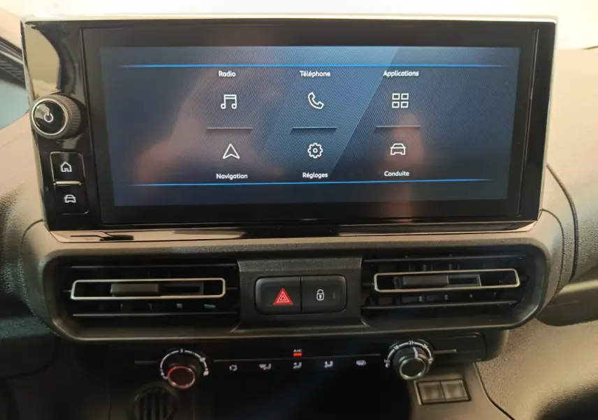 Écran tactile central du tableau de bord du Peugeot Partner 2025 avec commandes de climatisation et boutons de sécurité.