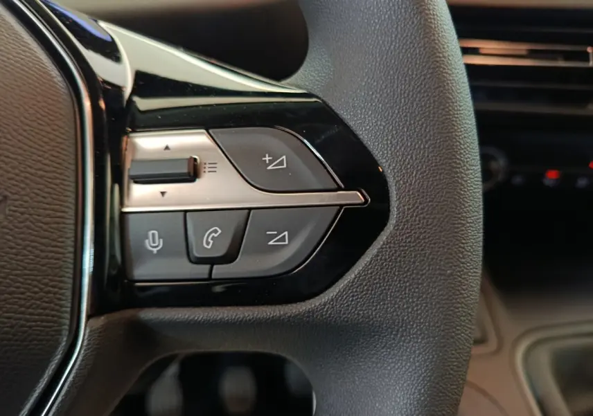 Gros plan sur les commandes noires et argentées au volant du Peugeot Partner blanc, côté gauche, intérieur moderne.