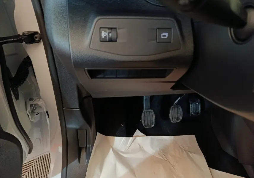 Vue intérieure en bas côté conducteur du Peugeot Partner blanc 2025, montrant les pédales et commandes sous le tableau de bord.