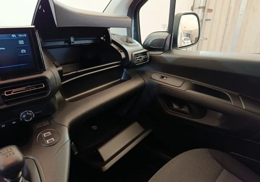 Vue intérieure côté passager du Peugeot Partner blanc 2025, avec boîte à gants ouverte et tableau de bord noir.