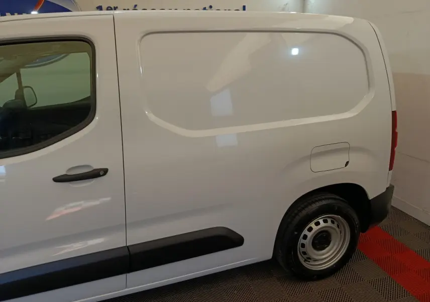 Vue de profil côté droit du Peugeot Partner blanc 2025, montrant la porte latérale pleine et la roue arrière acier.