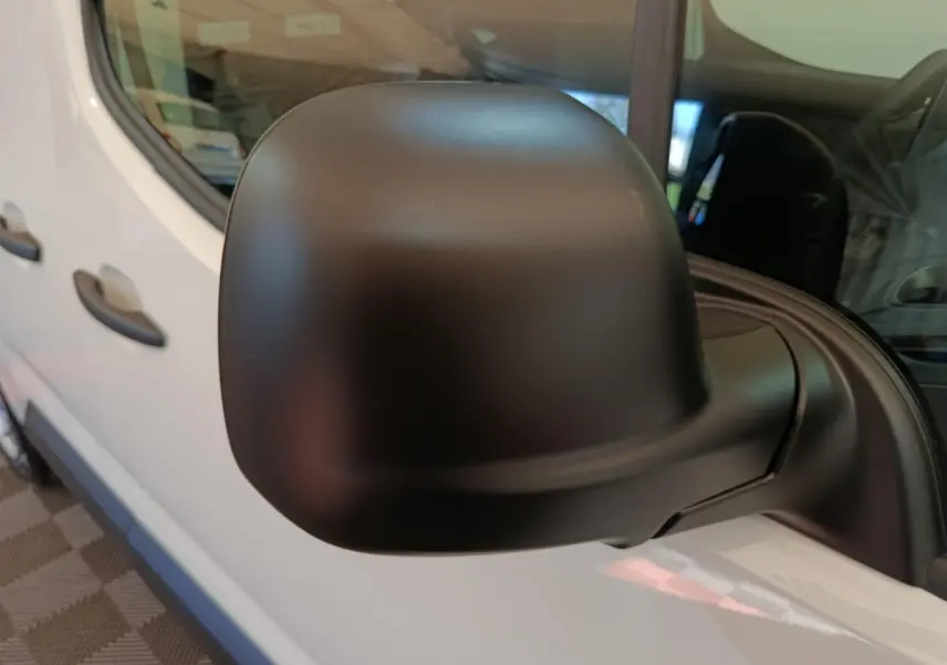 Gros plan sur le rétroviseur noir côté conducteur du Peugeot Partner blanc, avec vue partielle de la portière avant.