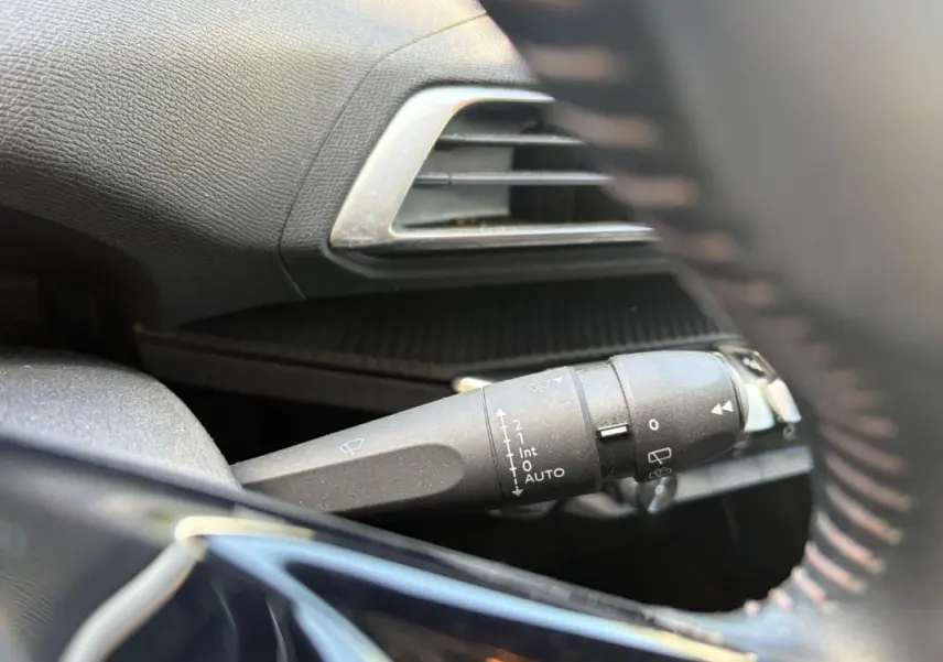 Gros plan sur la commande d’essuie-glace à gauche du volant d’un Peugeot 3008 noir, intérieur noir avec aérateur argenté.