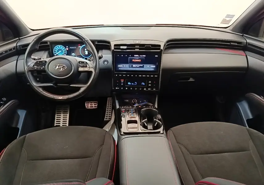 Vue intérieure frontale du Hyundai Tucson N Line 2022, tableau de bord noir avec écran tactile central et volant cuir multifonctions.